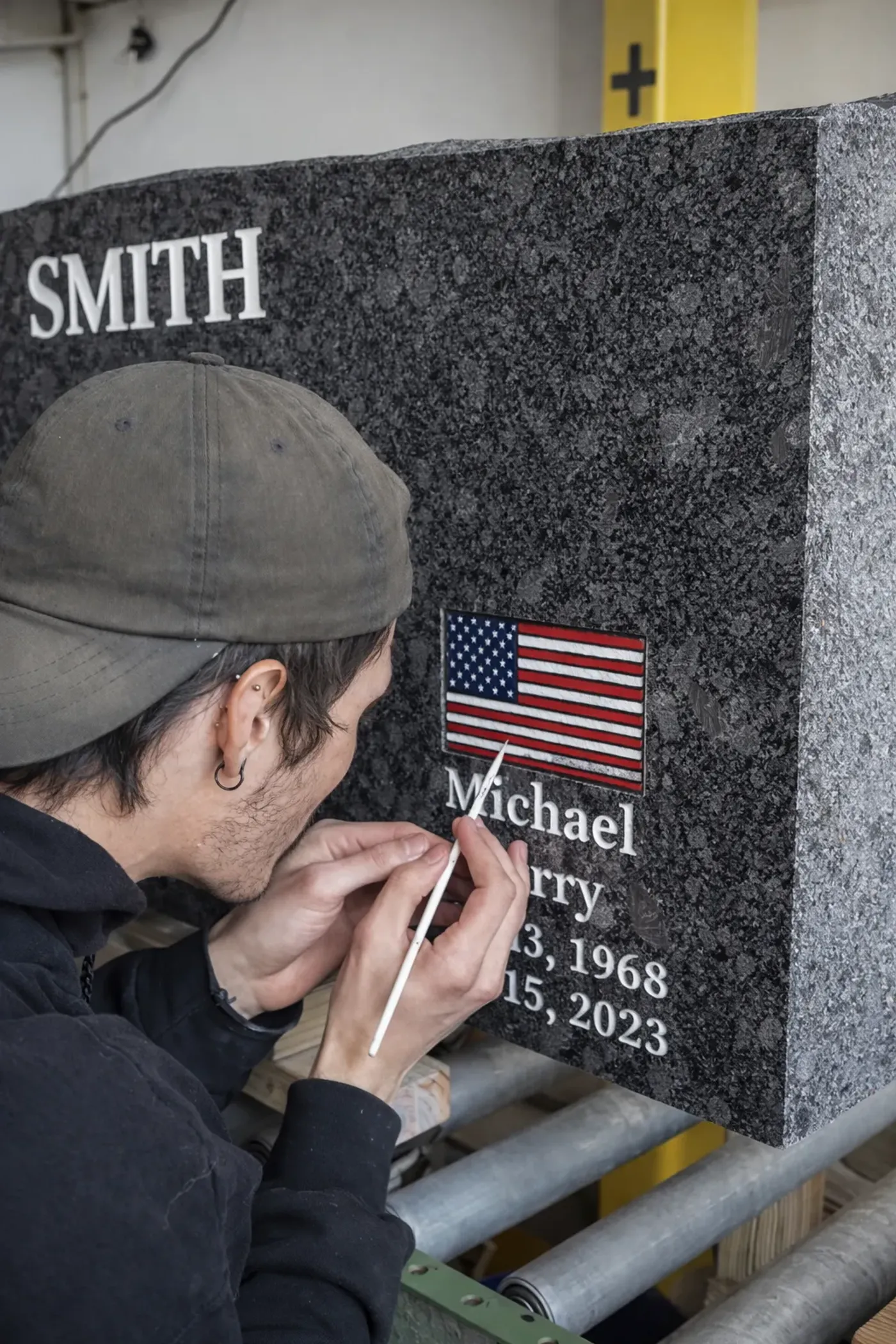 A Utah Headstone Design artist hand-painting an American flag detail on a granite headstone