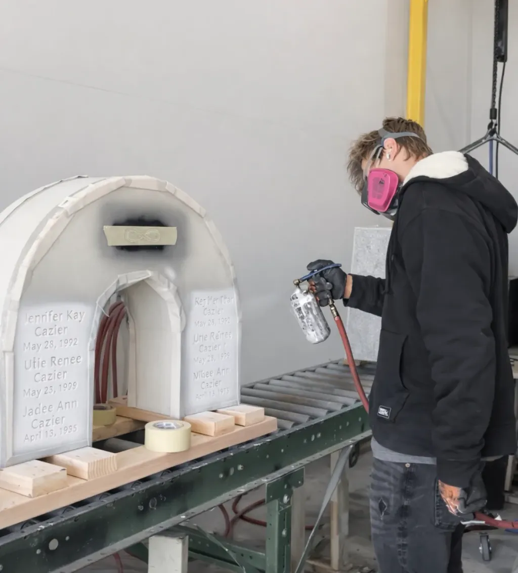A craftsman spray-coating an arched granite monument in the Utah Headstone Design finishing booth